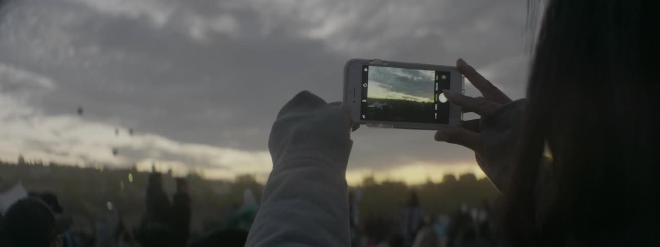 A woman is using a cellphone to photograph a scene at dusk