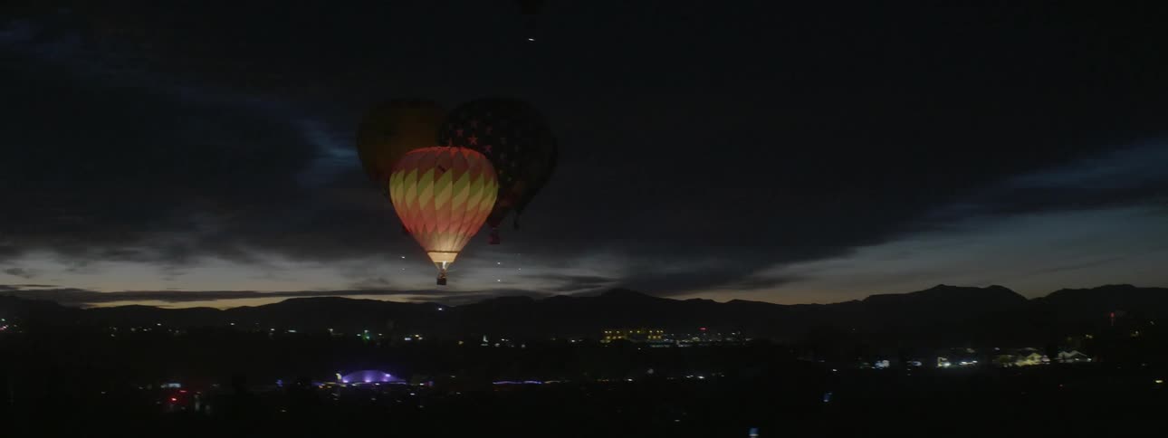 A few hot air balloons are lifting into the air at dusk