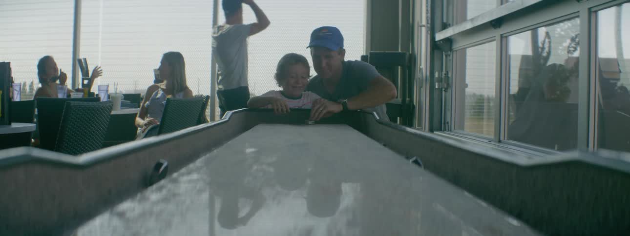 An older man and a young boy are playing air hockey