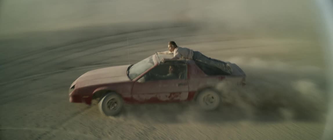 A man is riding on top of a vehicle as it speeds in circles in the desert