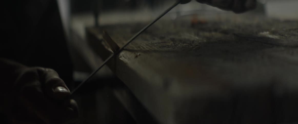 A man uses a long blade to strip wood