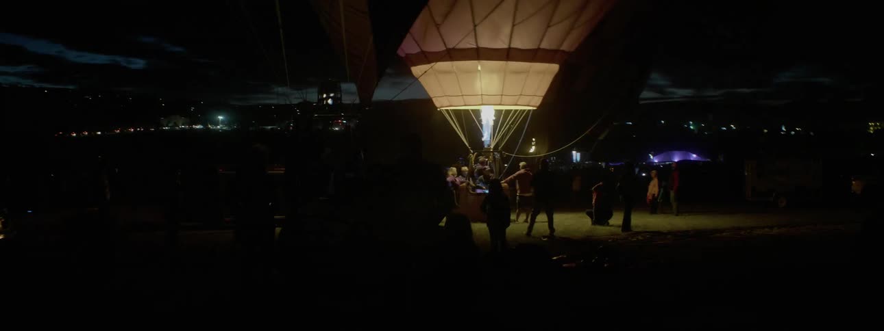 Hot air balloons are flashing there fire engines and glowing for people who are standing around watching