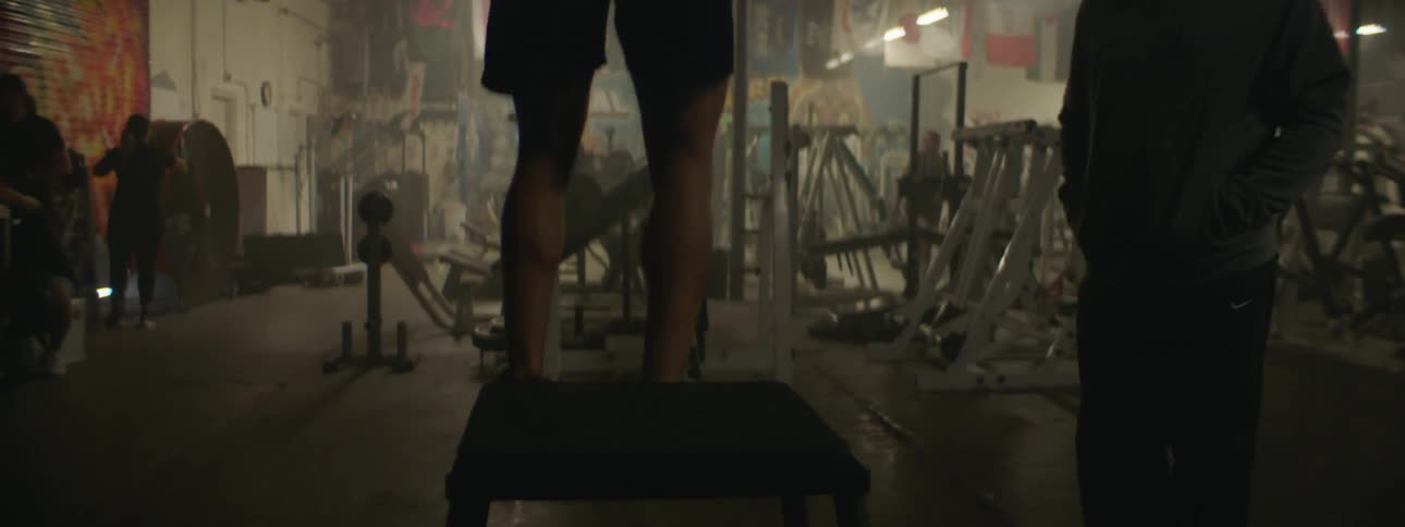 A man exercises in a gym by jumping onto a platform