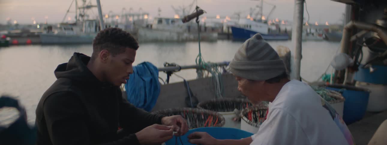 Two people are sitting on the dock tying string around a net