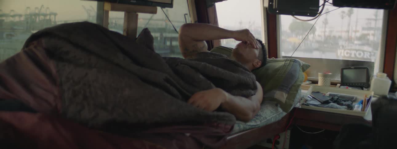 A man lying in a bunk on a boat is rubbing his eyes