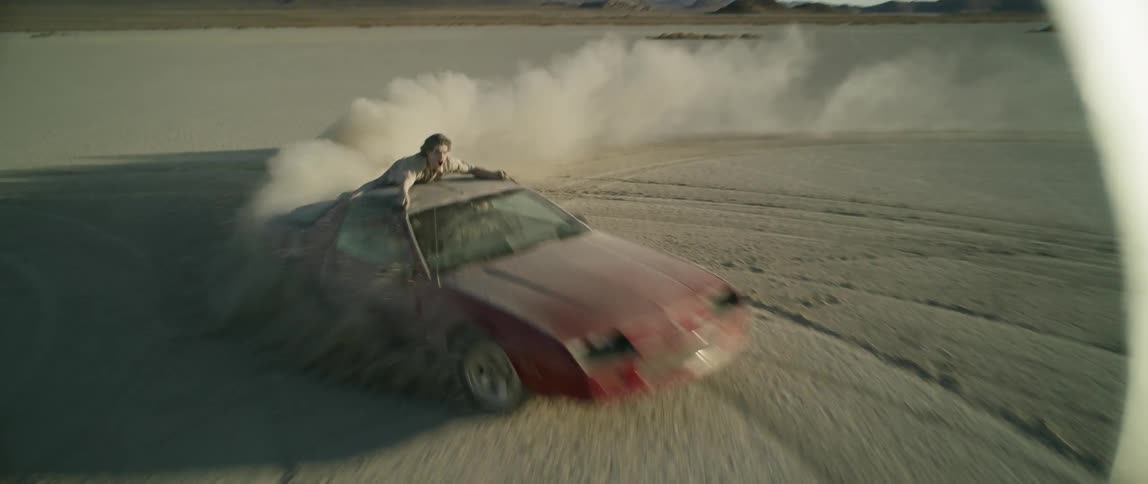 A man rides on top of a sports car while driving through the desert