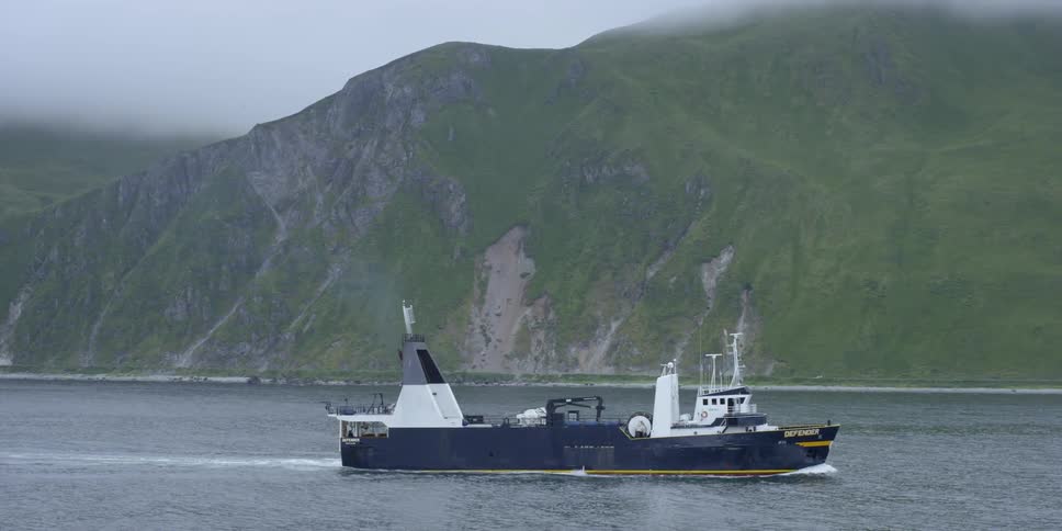 A ship is moving past a mountain coastline on a cloudy day