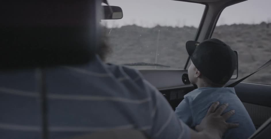 Man pats a boys back while driving a car