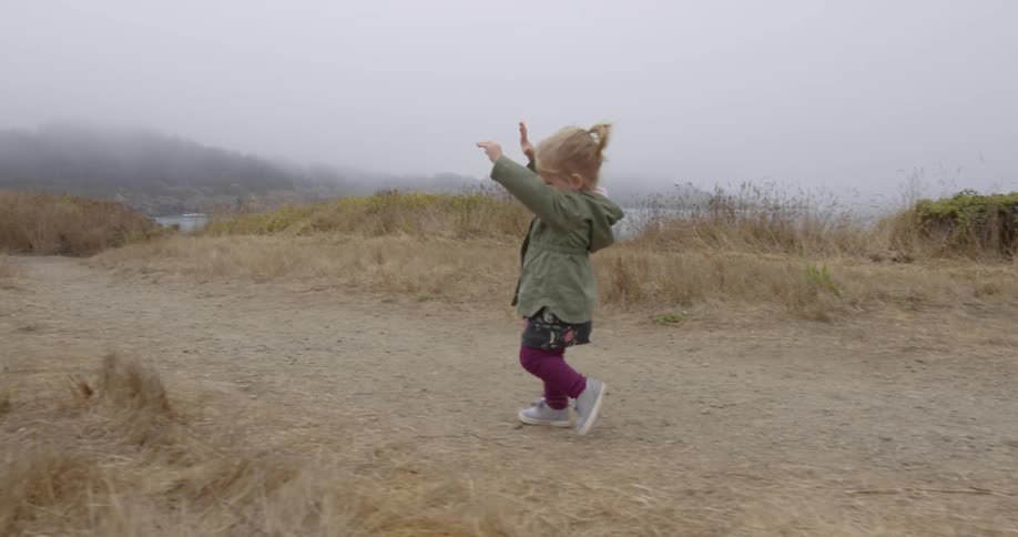 A little girl walks along a dirt path with her hands up
