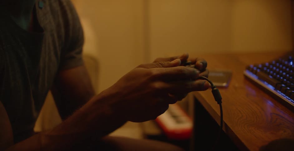 A man is sitting at a desk using a gamepad at night