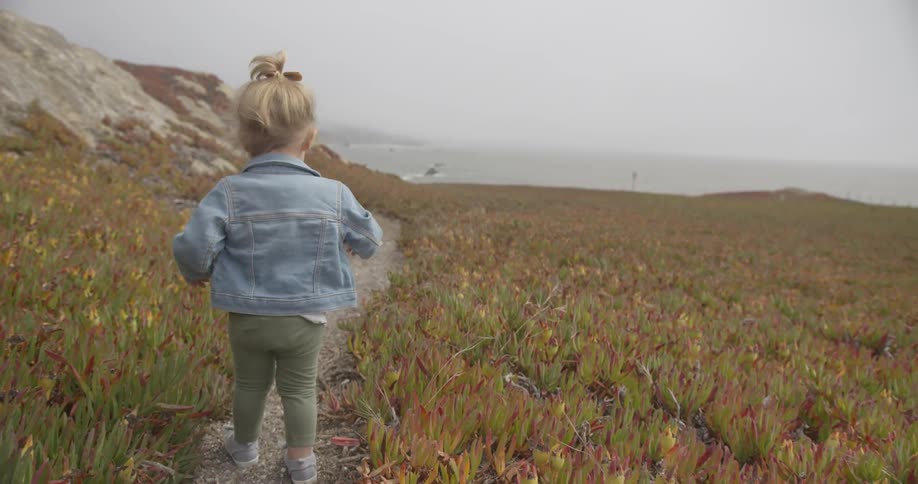 A toddler is walking down a dirt path