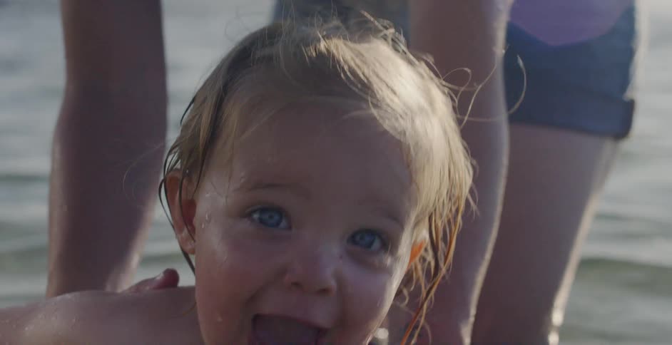 A toddler is being held and playing in the water at the beach