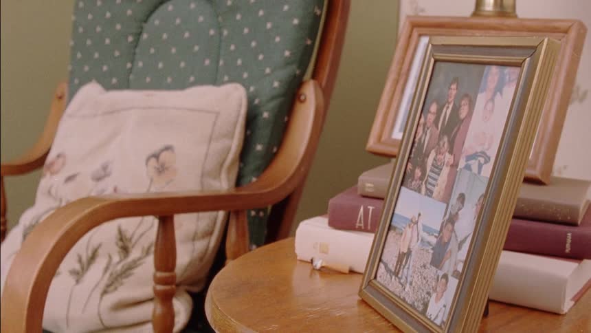 Framed photographs sit on a table next to a rocking chair
