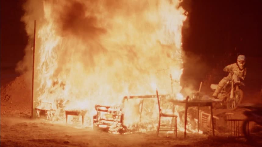 Dirt bike riders are riding around a large fire