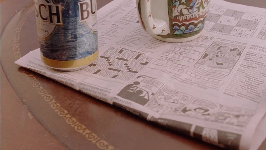 A beer can and coffee mug sit on top of a newspaper