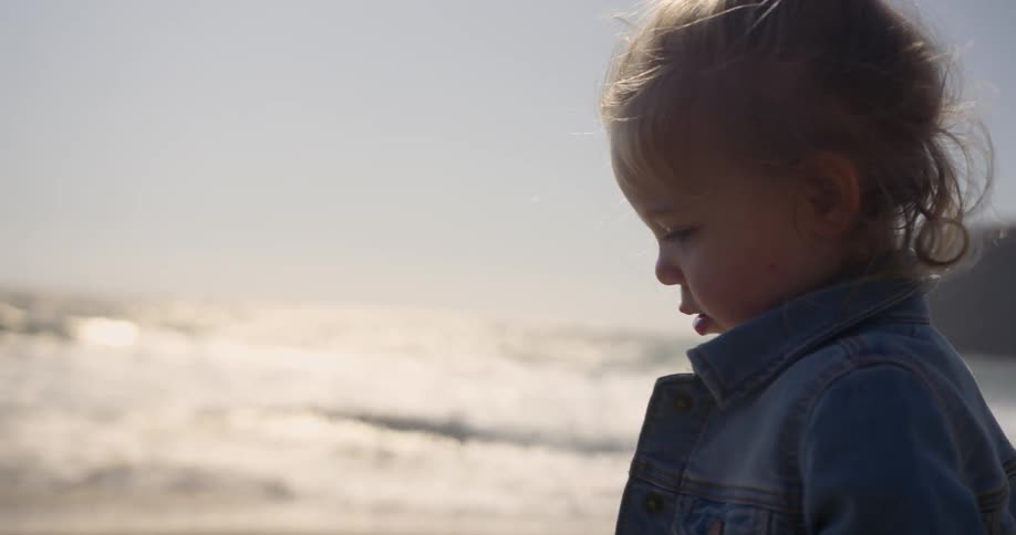 Toddler looking down on a beach as the sea roll in next to them