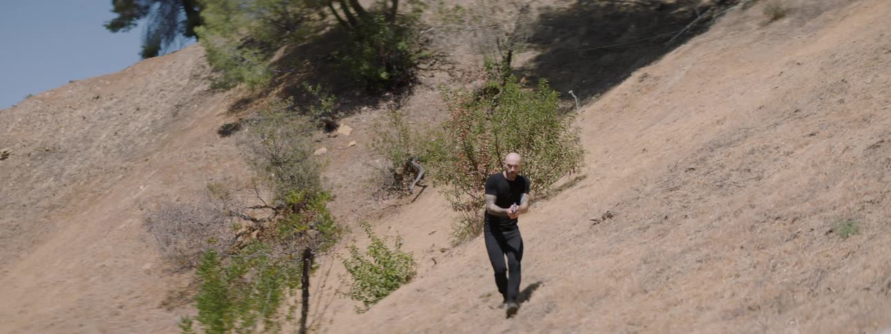 A man with a gun walks across a slope searching