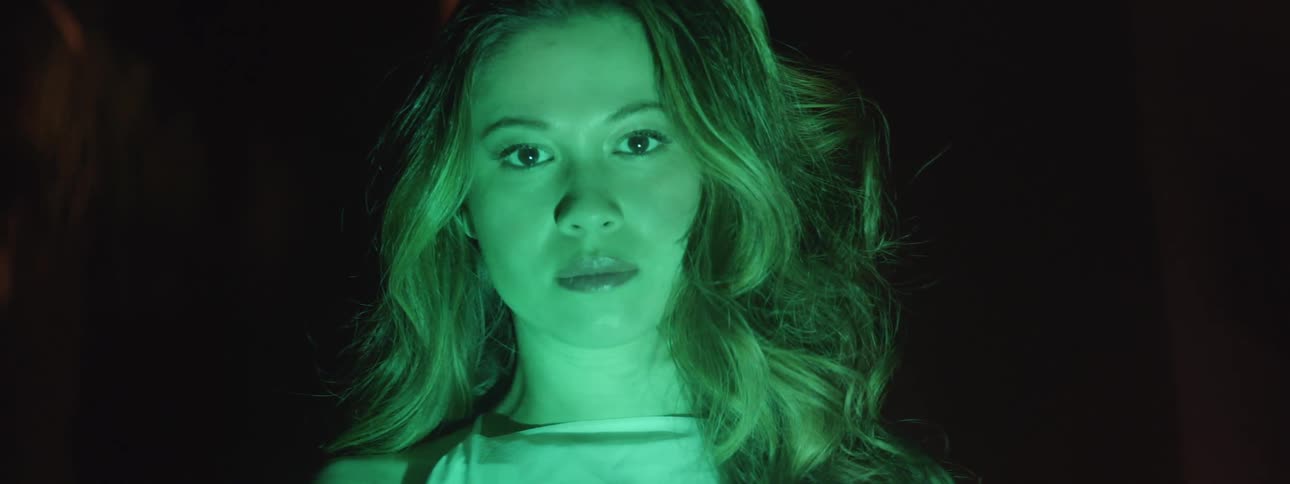 A woman bathed in green light stares blankly
