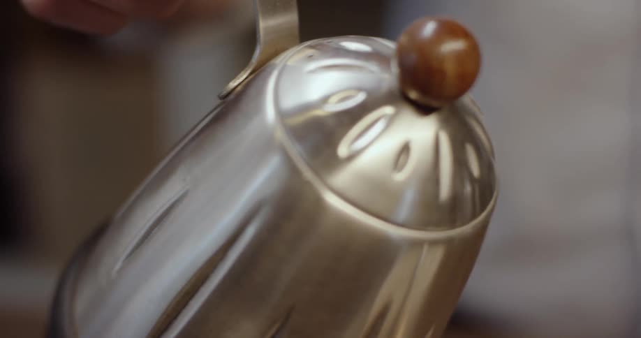 A hand is holding a water kettle as it is being poured