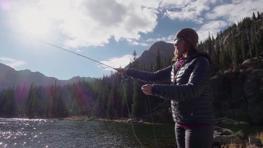 A woman is fly fishing on the shore of a lake