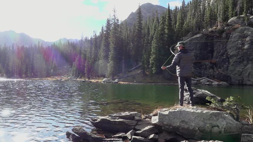 Man stands on a rock by a river and fly fishes