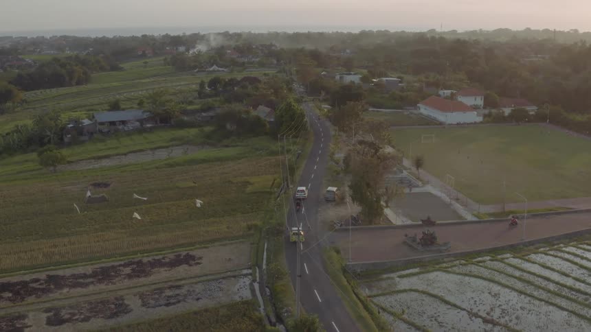 Cars drive past rows of farmland