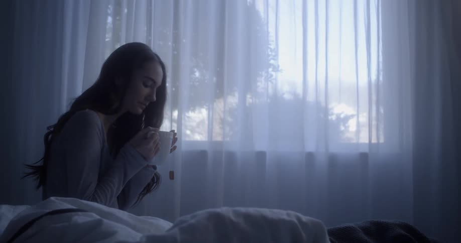 A woman takes a drink from her cup by the window