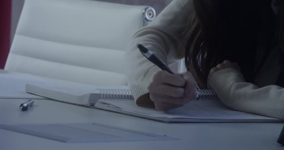 A woman writes in a notebook at a table