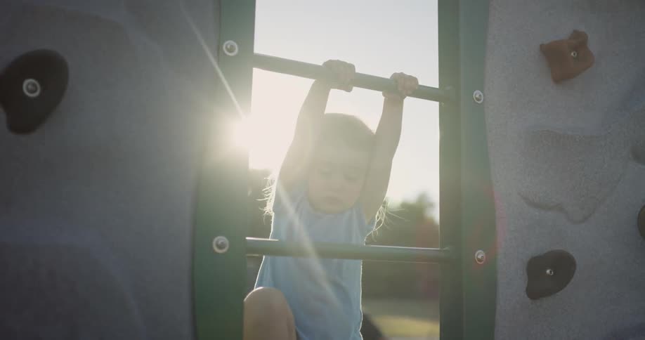 Little girl is climbing up a ladder on a park structure on sunny day