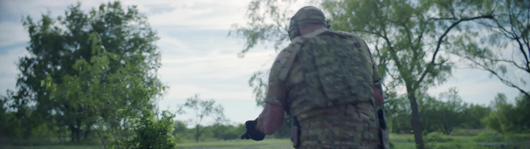 Soldiers walk through a rural area with guns