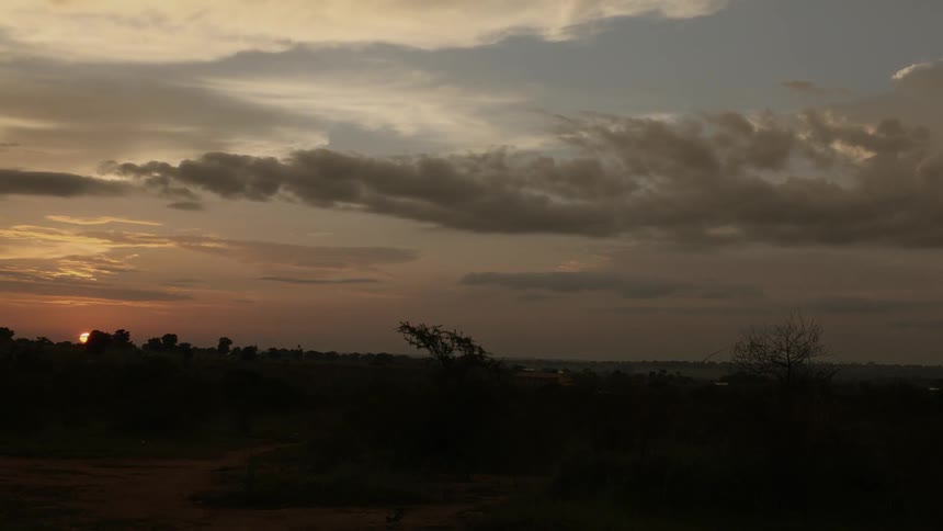 The sun sets over a desert as clouds float by