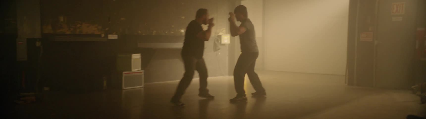 Two men fist fight in an empty room