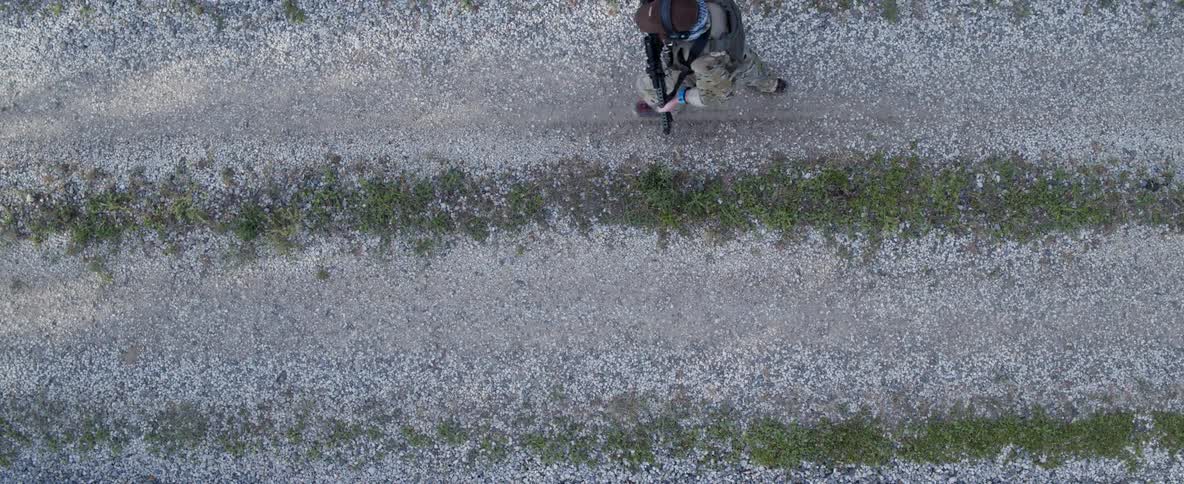 Man wearing camouflage and carrying rifle is running on a rocky road