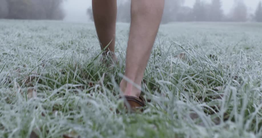 A person is walking in the frost covered grass