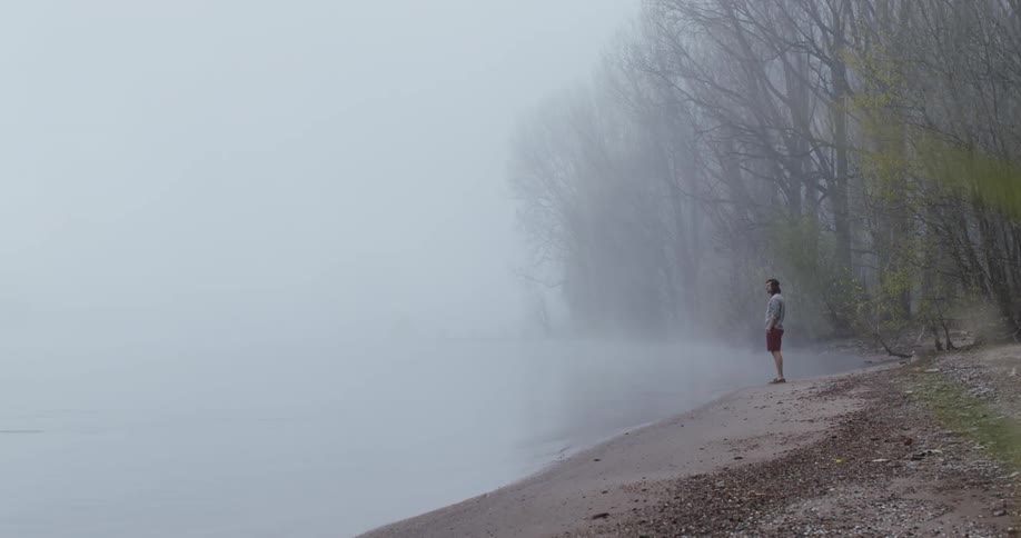 A man walks towards the foggy shore