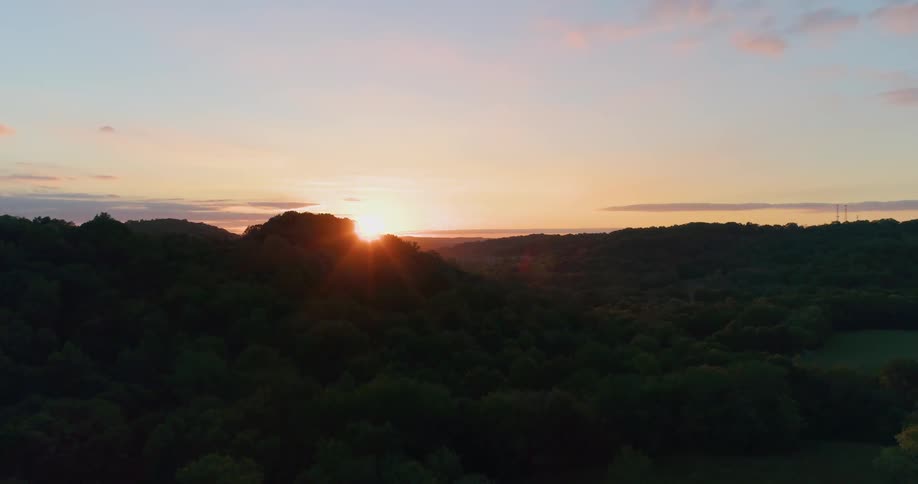 The sun sets over tree-covered hills