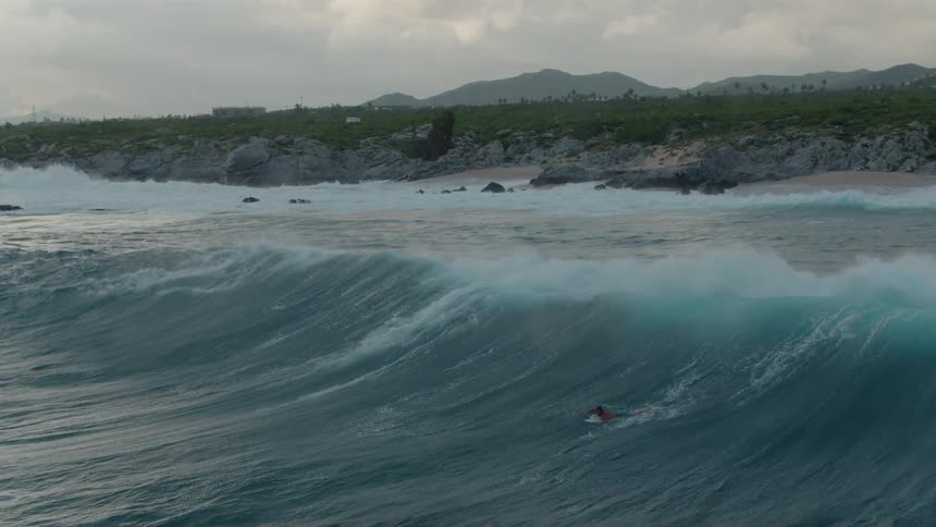 A surfer floats on an ocean wave at sunset