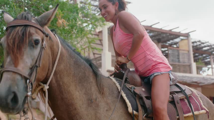 Woman mounting a horse on its saddle and then petting its neck