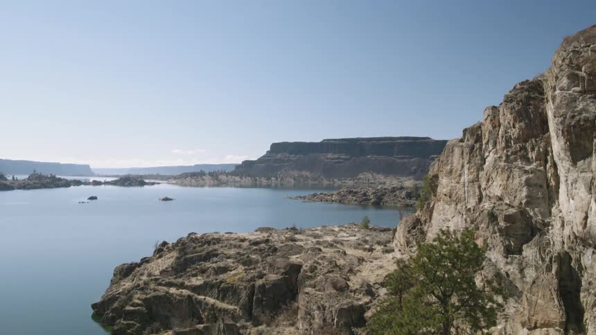 Ascending a rugged lakeshore rock wall with blue water surrounded by tall plateaus in the distance