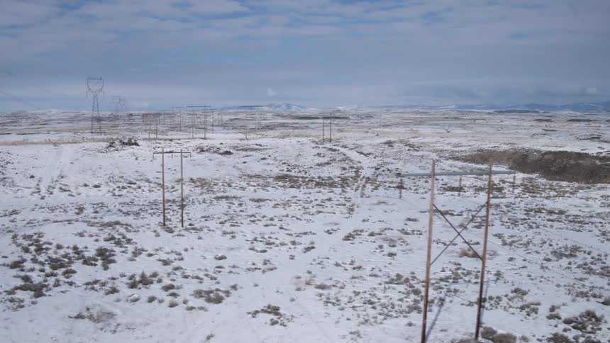 Flying close to a large installation of high voltage power lines that stretch across a snow covered landscape