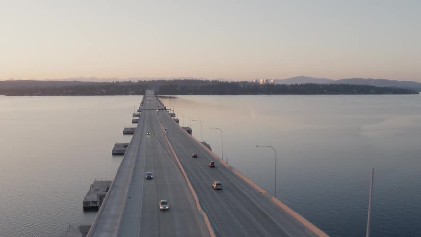 Orbiting around light traffic crossing over a long concrete bridge at sunrise