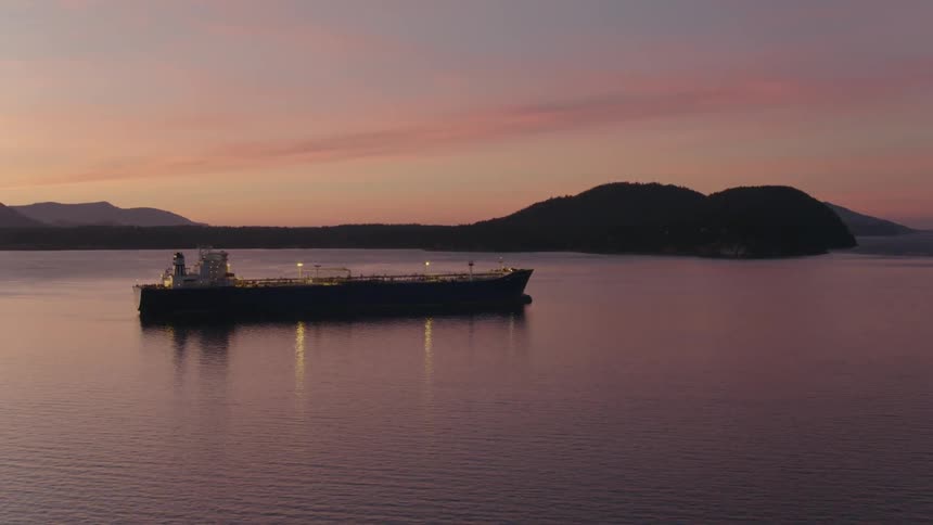 Approaching a large oil tanker moored in a calm bay at sunset