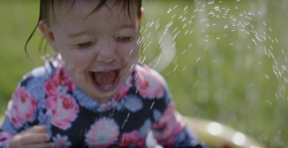 A toddler girl smiles while playing in water in a backyard