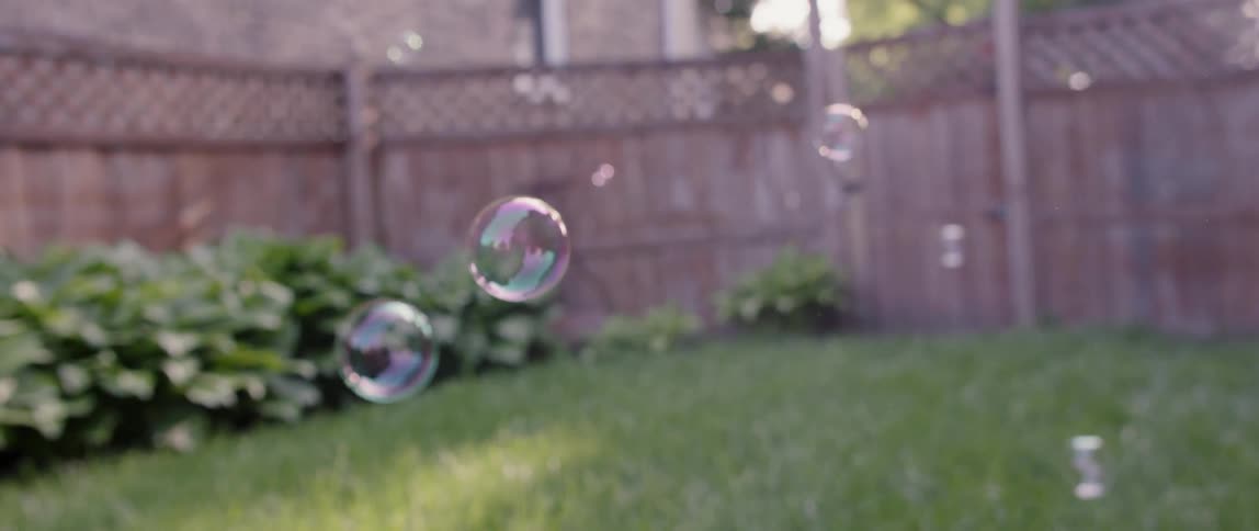 Bubbles are floating through the air in a backyard during the day