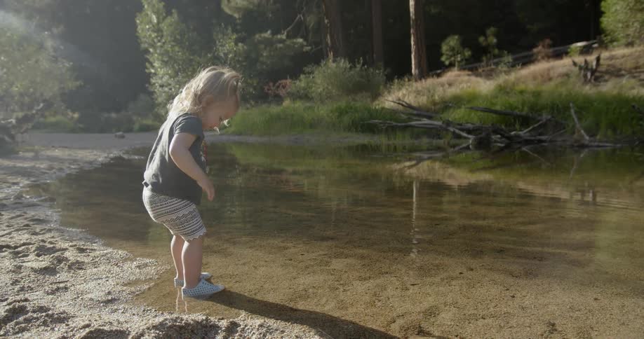 A toddler girl stands in a stream