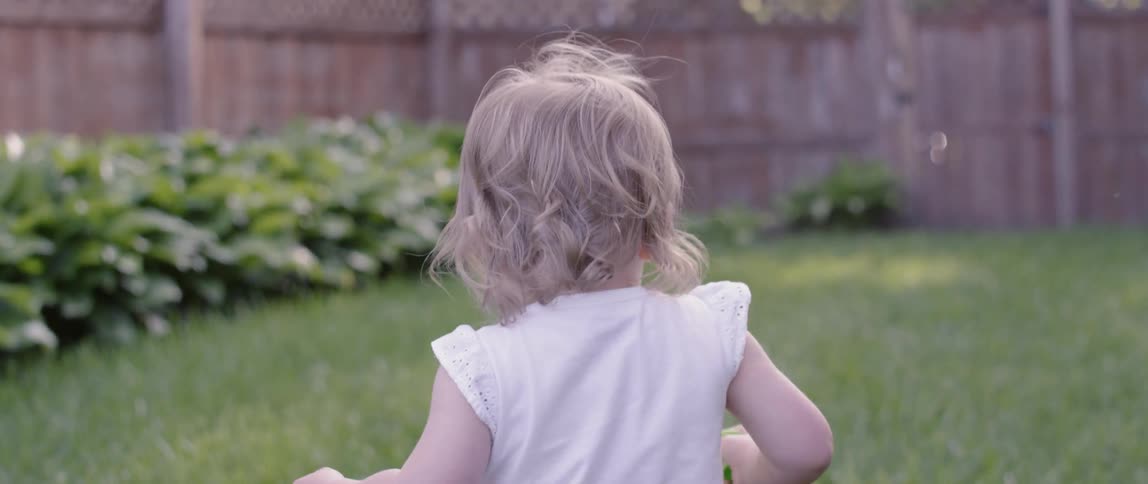A toddler girl walks in a grassy backyard