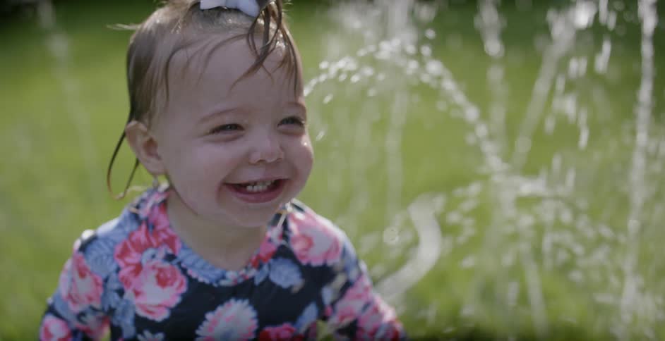 A toddler girl is playing in water in a backyard during the day