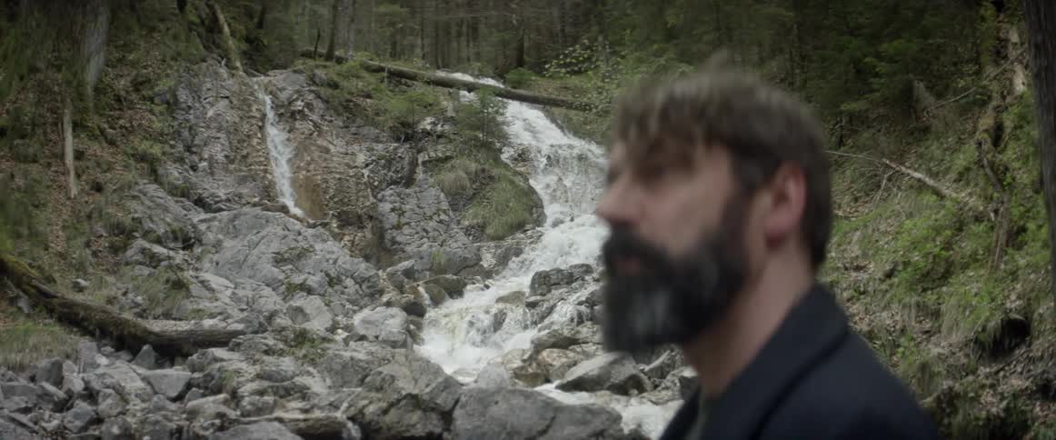 A man looks around at nature by a stream