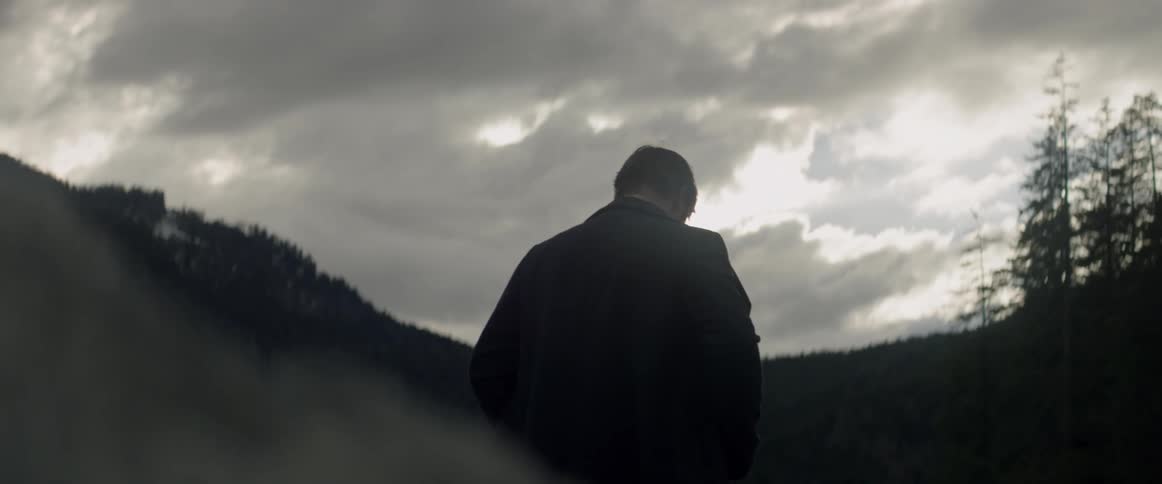 A man stands outside under the clouds and looks downward