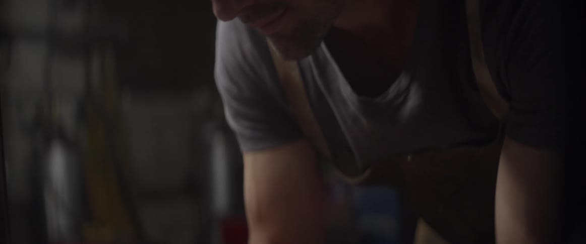 A man in an apron bends over a workshop table with a pen